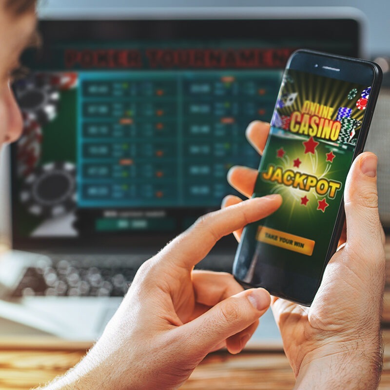 un'immagine che ritrare un utente mentre gioca a giochi di casino da cellulare con un pc sullo sfondo