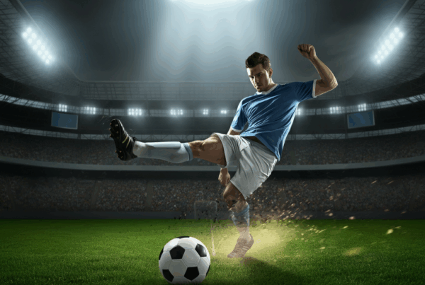 Un calciatore mentre calcia su un campo verde illuminato, simbolo dell'energia e della tensione intorno alle quote vincente conference league, con uno stadio e pubblico sfocato sullo sfondo.