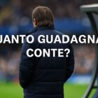 Antonio Conte di spalle davanti a una panchina su un campo da calcio, illuminato dai riflettori di uno stadio, con la scritta Quanto guadagna Conte? in alto.