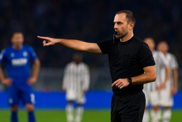 immagine che mostra un Arbitro di Serie A di tre quarti con un fischietto in mano che indica il centro del campo, circondato da giocatori pronti alla ripresa del gioco sotto le luci dello stadio, durante una partita serale — scena che illustra quanto guadagna un arbitro di Serie A per descrivere un articolo che spiega quanto guadagna un arbitro in serie a