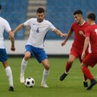 Stipendi giocatori Serie C Quattro calciatori in azione durante una partita di calcio su un campo verde, due in maglia bianca e due in maglia rossa, che si contendono il pallone in uno stadio vuoto, con sfondo leggermente sfocato e atmosfera dinamica in rappresentanza di quanto guadagna un giocatore di serie b