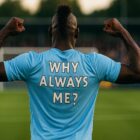 Giocatore di calcio di colore, visto di spalle su un campo da calcio, con cresta e posa muscolare, indossa una maglia con la scritta “Why Always Me?”, immagine ispirata alla celebre esultanza di Mario Balotelli e al concetto dove gioca Balotelli.