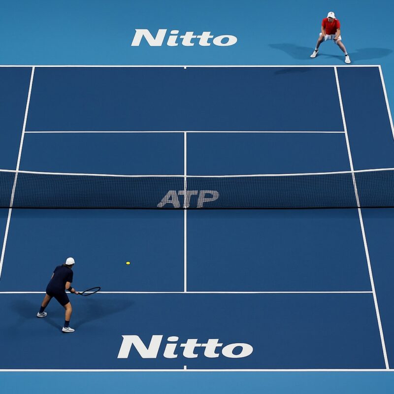 Veduta dall’alto di un campo blu delle ATP Finals con due giocatori non riconoscibili durante il match, immagine riferita a Sinner in semifinale ATP Finals 2025.