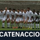 Durante una partita di calcio, dieci giocatori si posizionano davanti alla porta formando una barriera difensiva compatta, simbolo del catenaccio. Nella parte inferiore dell’immagine compare la scritta 'Catenaccio', rappresentando visivamente che cos’è il catenaccio nel calcio