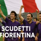 Giocatori della Fiorentina in maglia viola festeggiano in campo con il pugno alzato davanti a una grande bandiera italiana, rappresentazione celebrativa dei due Scudetti Fiorentina.