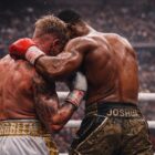 Due pugili di spalle in clinch al centro del ring, corpi tesi e guantoni serrati, scena simbolo di un match durissimo concluso per KO in rappresentanza del match Jake Paul vs Joshua