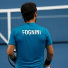 Fabio Fognini di spalle su un campo da tennis blu, in maglia azzurra con scritta “FOGNINI”, racchetta in mano e rete sullo sfondo. la foto fa riferimento all'intervista di Fognini a Belve