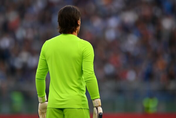 Portiere di calcio di spalle in divisa verde fluo, guanti bianchi e neri, fermo in campo con lo stadio sfocato sullo sfondo che rappresenta l'articolo del blog di quogioco Quanto guadagna Sommer