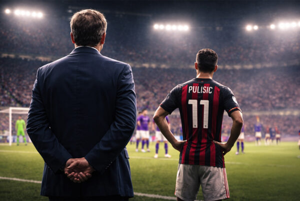 Capello di spalle a bordo campo osserva il Milan in partita sotto le luci dello stadio, con giocatore rossonero sul terreno di gioco.