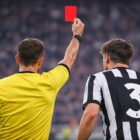 Arbitro di spalle mostra un cartellino rosso a un calciatore in maglia bianconera numero 3 durante una partita.