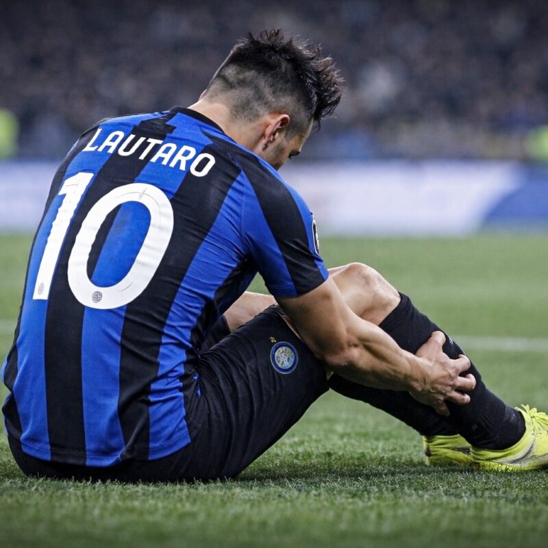 Calciatore seduto sul campo da calcio di spalle mentre si tiene il polpaccio dolorante dopo un infortunio in rappresentanza di inter lautaro infortunio