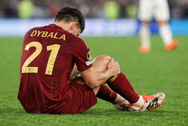 Nuovo Infortunio Dybala: Paulo Dybala di spalle seduto sul campo mentre tiene il ginocchio dolorante durante una partita della Roma.