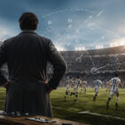 Allenatore di spalle osserva la squadra in campo mentre applica il movimiento calcio durante una partita in uno stadio affollato