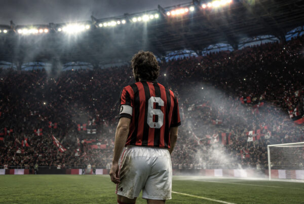 Franco Baresi di spalle con la storica maglia numero 6 del Milan osserva lo stadio illuminato, in un'illustrazione iperrealistica che rende omaggio alla leggenda del calcio italiano.