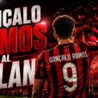 Gonçalo Ramos al Milan rappresentato in una grafica editoriale con un calciatore di spalle che saluta i tifosi rossoneri sugli spalti, bandiere rosse e nere e il titolo "Gonçalo Ramos al Milan" in evidenza.