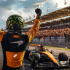 GP Ungheria 2026, pilota McLaren festeggia di spalle dopo la vittoria sul circuito con monoposto e tribune sullo sfondo.