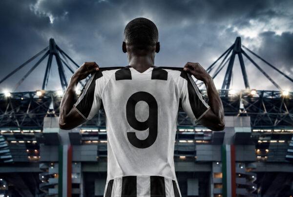 Kolo Muani Juventus di spalle con la maglia numero 9 nello stadio illuminato, immagine sportiva iperrealistica che rappresenta il nuovo centravanti bianconero.