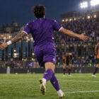 Venezia Fiorentina 2-4, calciatore viola di spalle festeggia sul campo sotto i riflettori.