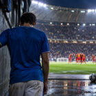 Italia-Belgio 0-2, calciatore azzurro di spalle nel tunnel dello stadio mentre i giocatori belgi festeggiano sul campo.