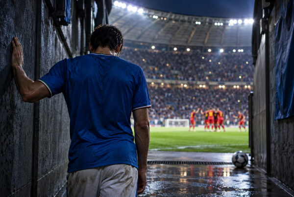 Italia-Belgio 0-2, calciatore azzurro di spalle nel tunnel dello stadio mentre i giocatori belgi festeggiano sul campo.